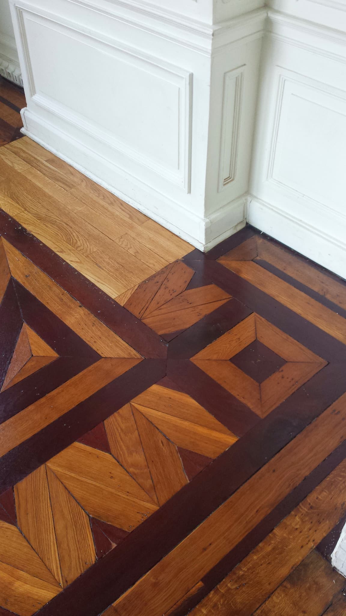 Motifs géométriques du parquet au pied de boiseries blanches.
