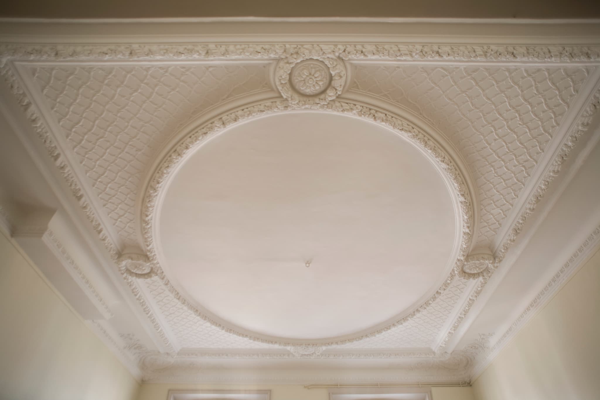 Détail d’un plafond blanc à moulures et médaillon ovale.