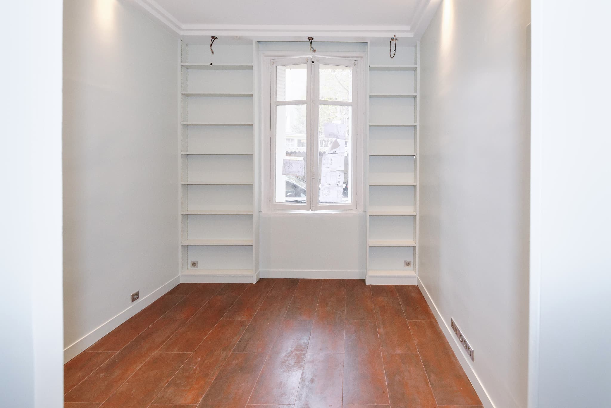 Rangements blancs de part et d’autre d’une fenêtre ; finitions en cours.