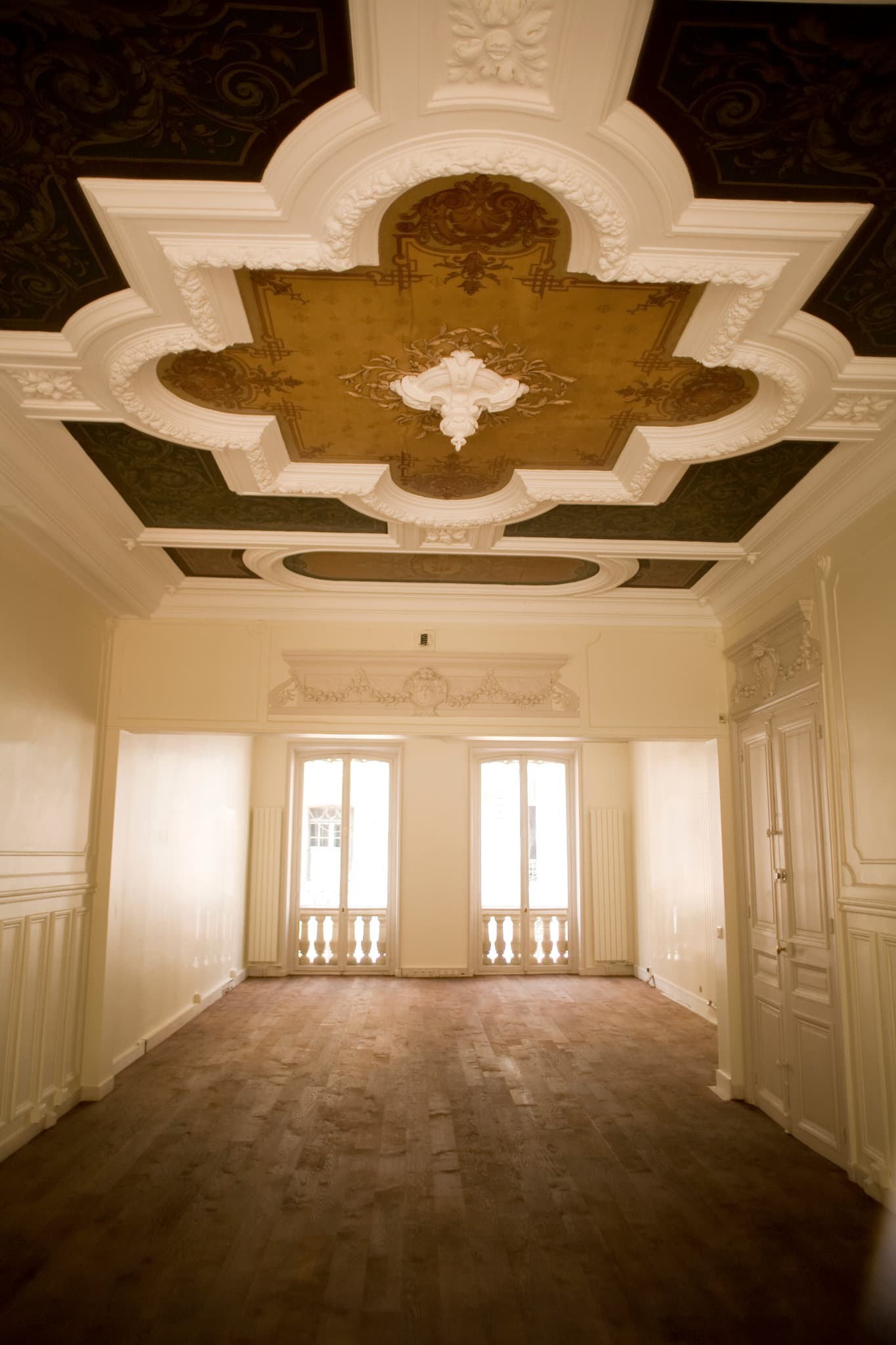 Volume intérieur sous un plafond peint, avec moulures blanches et parquet.